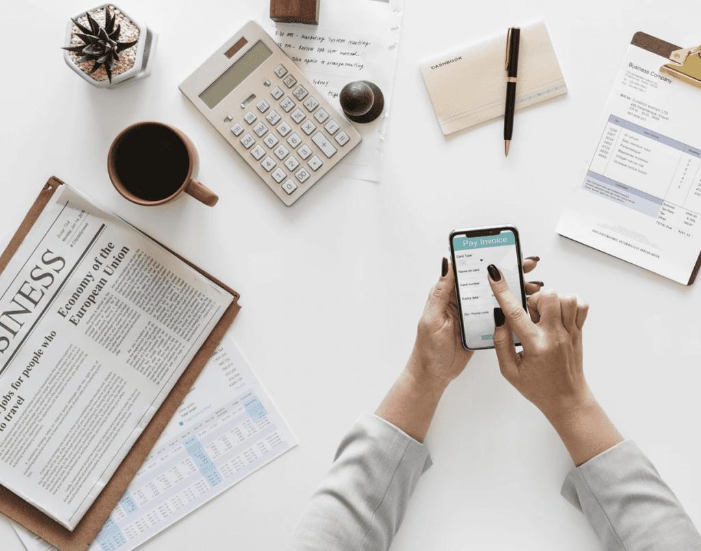 flat lay of woman using mobile phone with newspaper and business office items in background