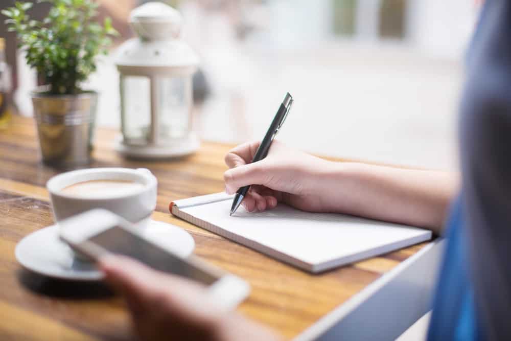 writing notes on paper with coffee and a phone