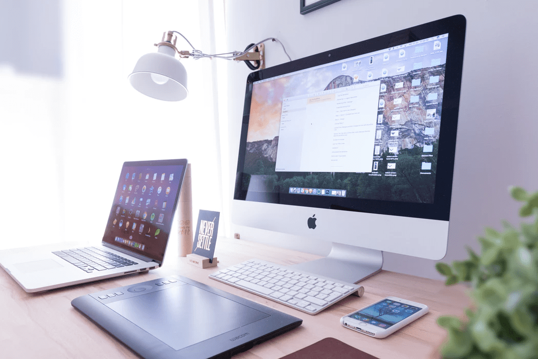 a productive work desk with laptop, desktop, phone and tablet