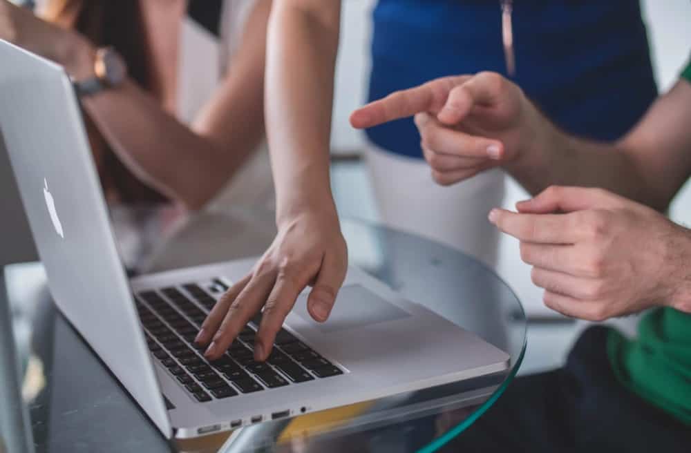 Arms and hands around and on a laptop situated on a glass table