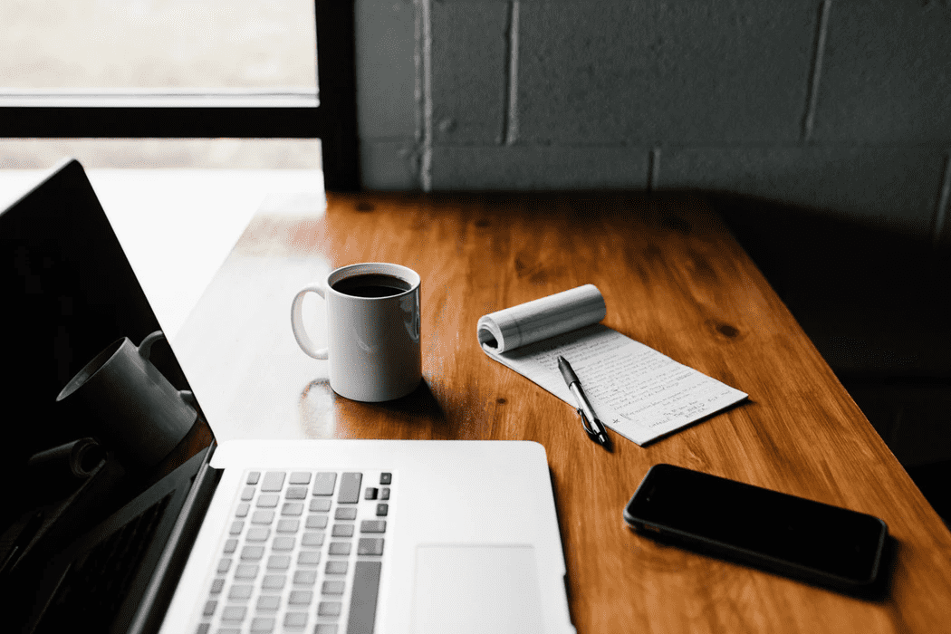 laptop, coffee mug, notepad, phone on a wooden table