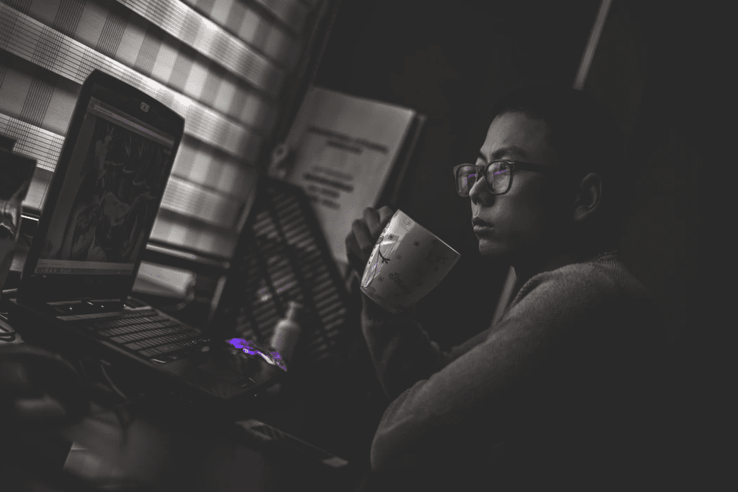 Manager drinking coffee and looking at his laptop, contemplating employee satisfaction