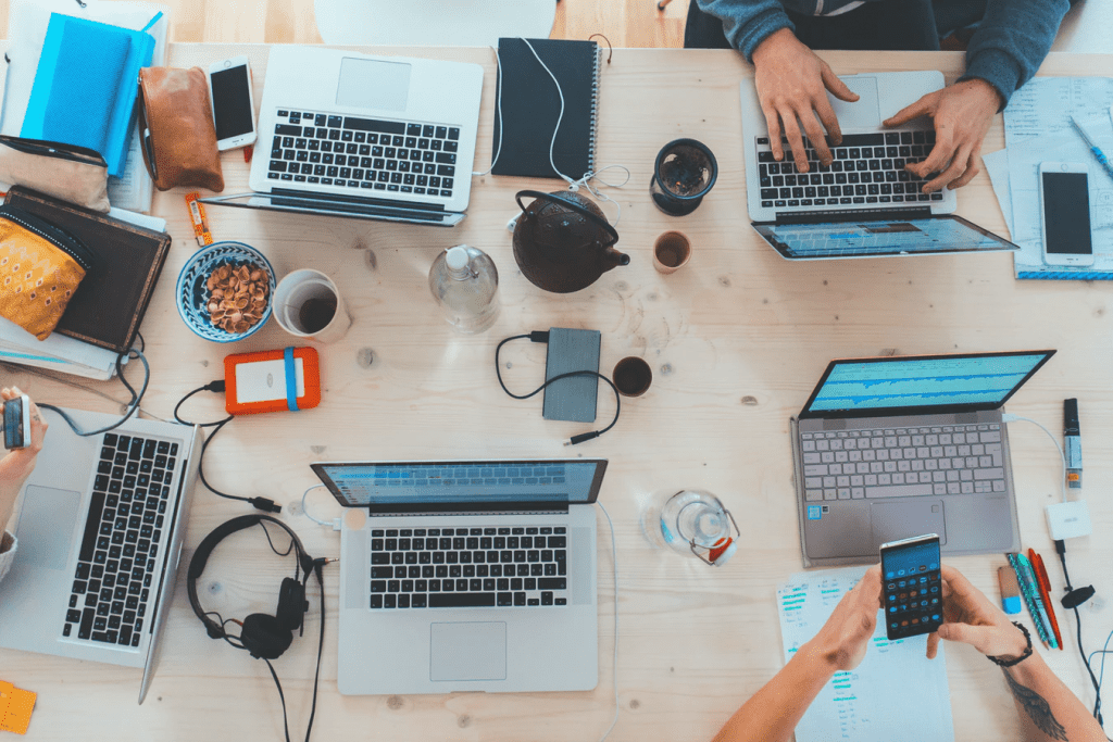 A table filled with BYOD like laptops, cellphones, and tablets that employees are working on