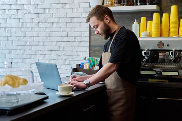 Owner coffee shop worker young male with laptop on the counter